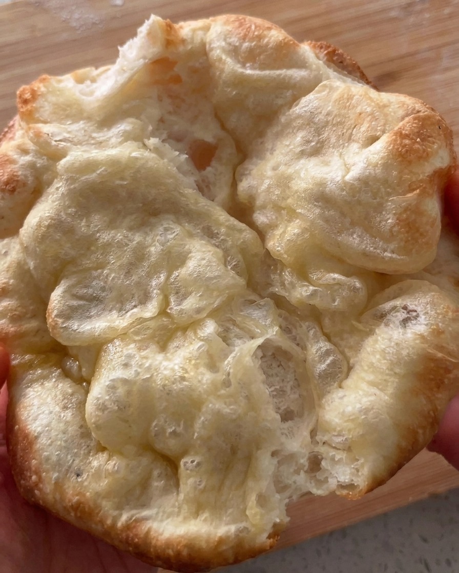 Freshly baked and blistered folded pizza bread being pulled open.