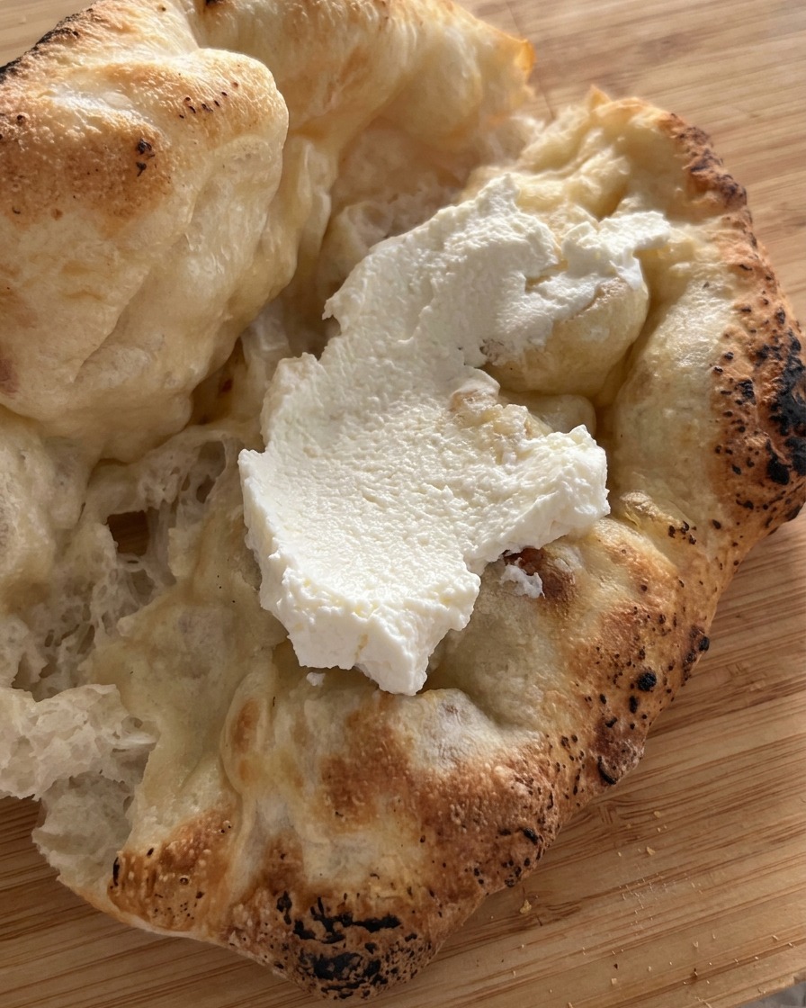 A thick layer of white ricotta cheese placed inside an opened, freshly baked pizza bread.