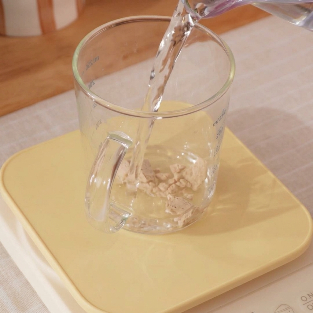 Close-up of a measuring cup with ice water and yeast being mixed with a small whisk.