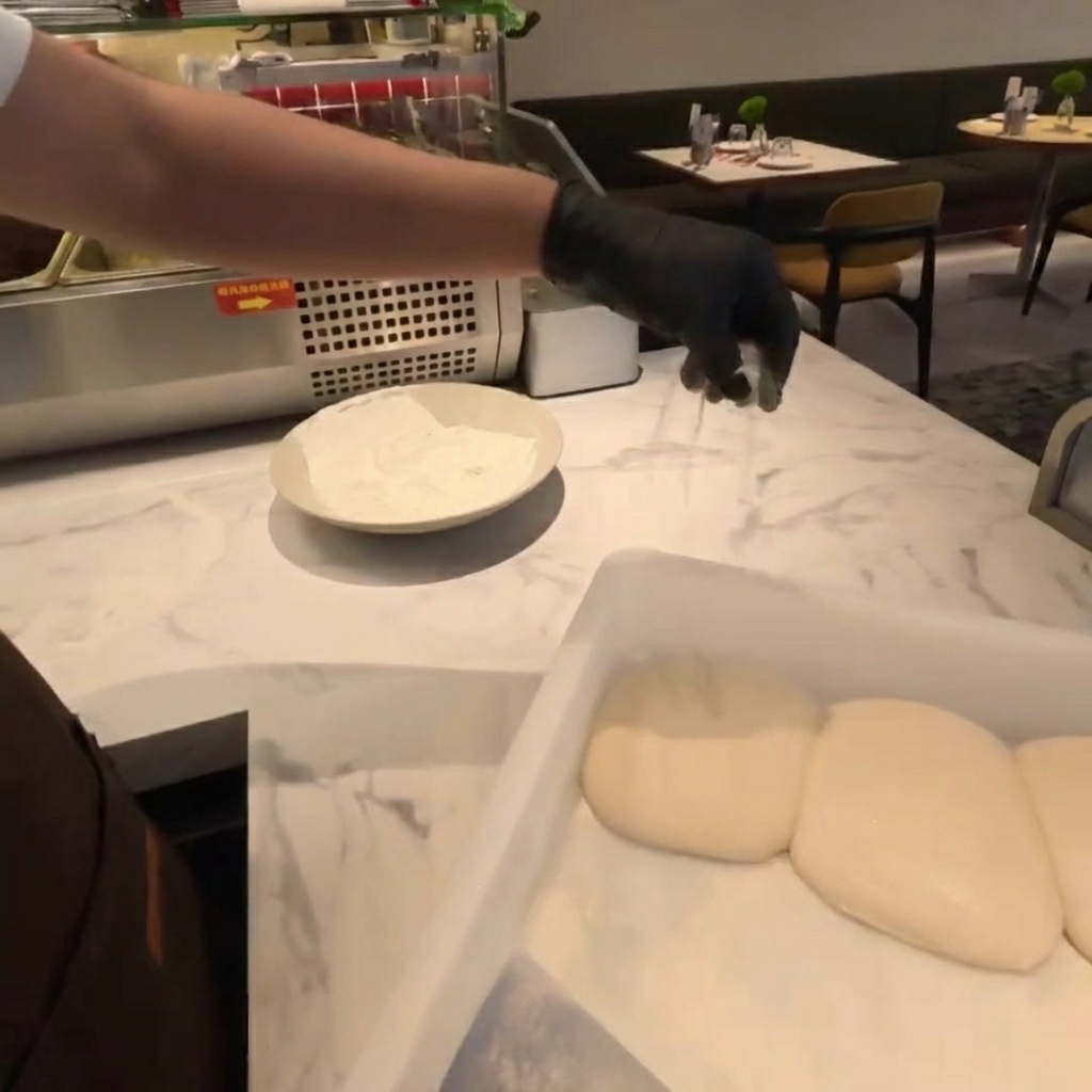 Flour being sprinkled over fresh dough balls on a marble countertop.