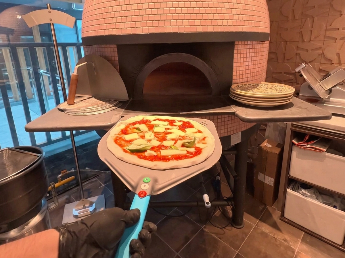 A pizza on a metal peel being placed into a traditional wood-fired brick oven.