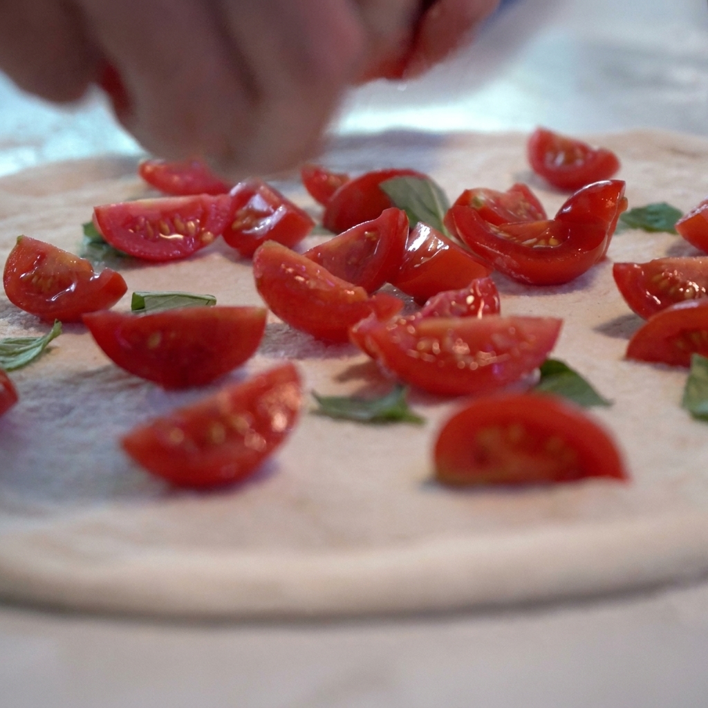 Tomato sauce and sliced fresh tomatoes being added to the raw pizza dough base.