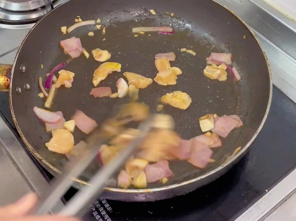 A mix of chicken, bacon, mushrooms, and onions being tossed in a hot pan.
