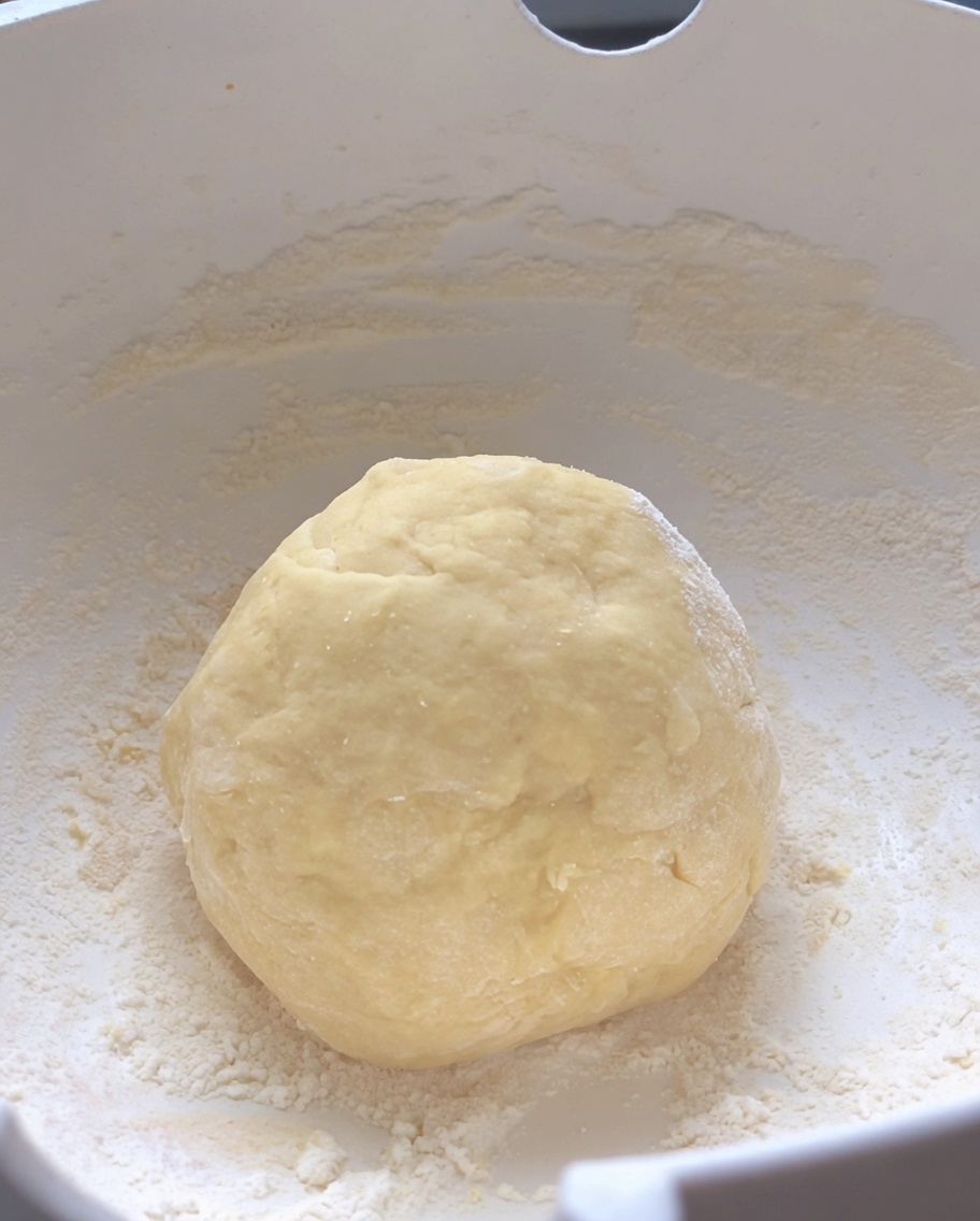 A smooth, round ball of kneaded raw dough resting in the center of a white mixing bowl.