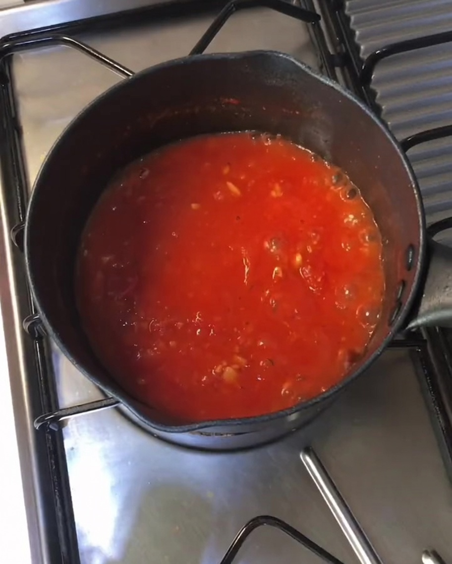 Thick, bubbling red tomato sauce simmering in a black pot on a stovetop.