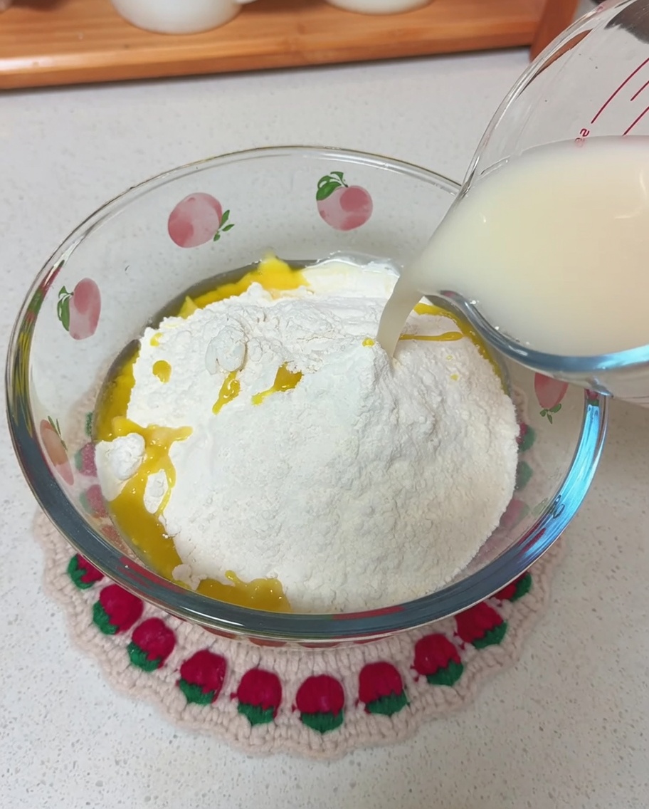 Pouring a milky yeast and water mixture from a glass measuring cup into a bowl of dry flour and olive oil.
