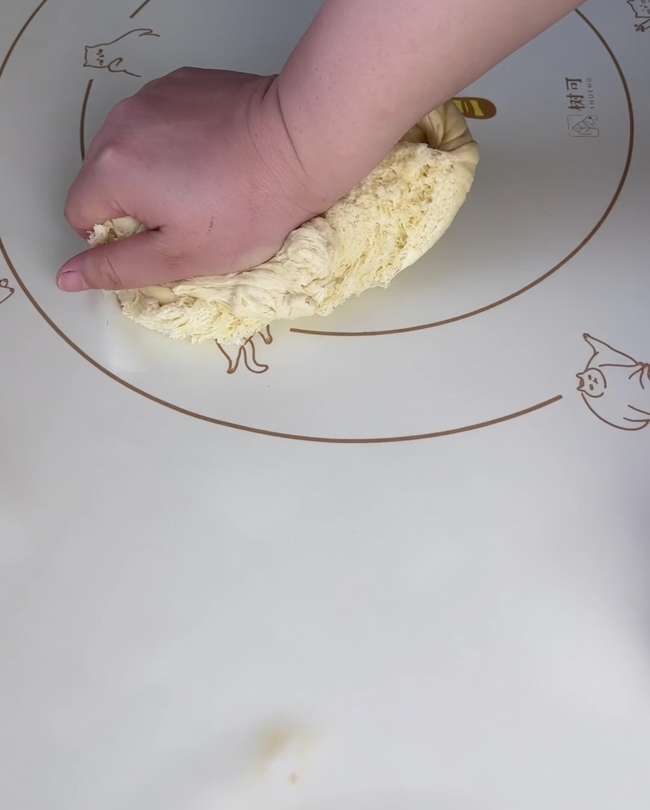 A hand pressing firmly on a piece of proofed dough on a patterned silicone mat to push out the air.