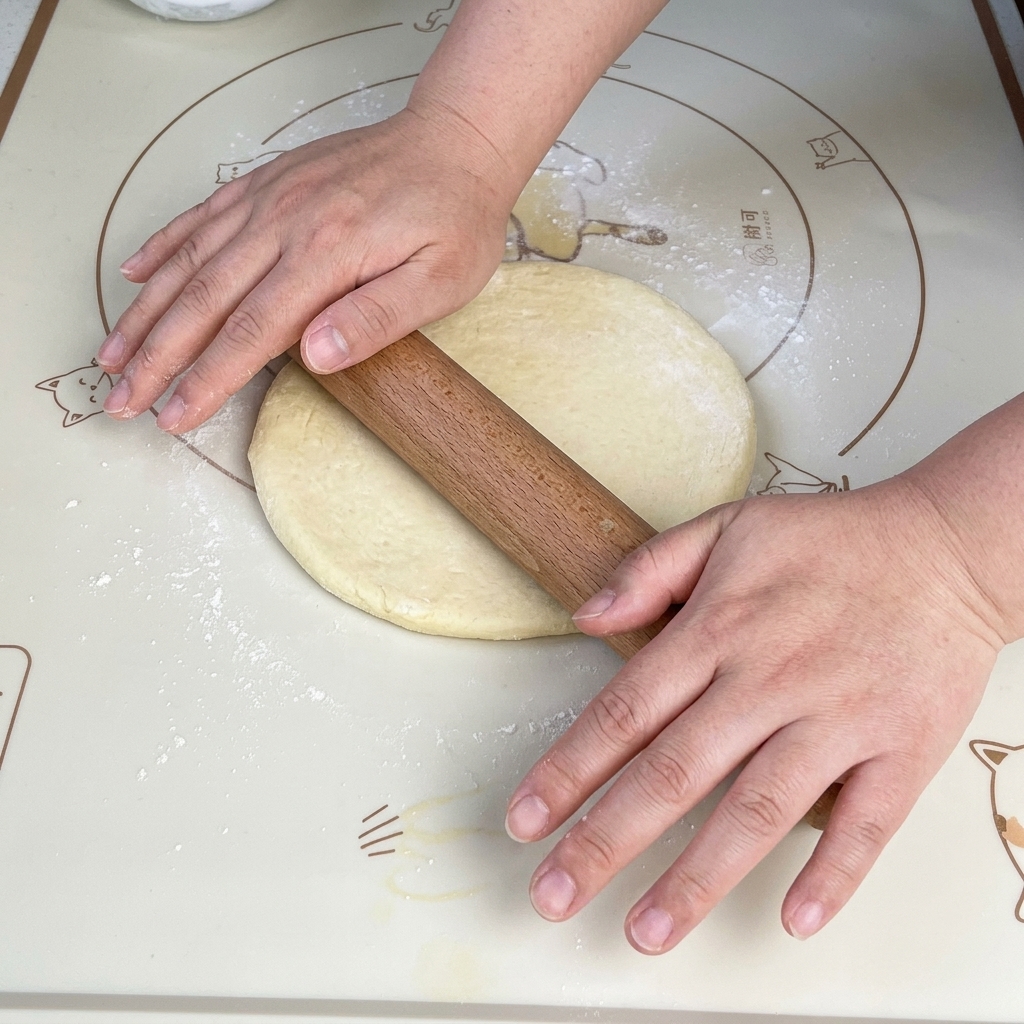 A wooden rolling pin flattening a soft piece of pizza dough into a uniform square shape on a non-stick baking mat.