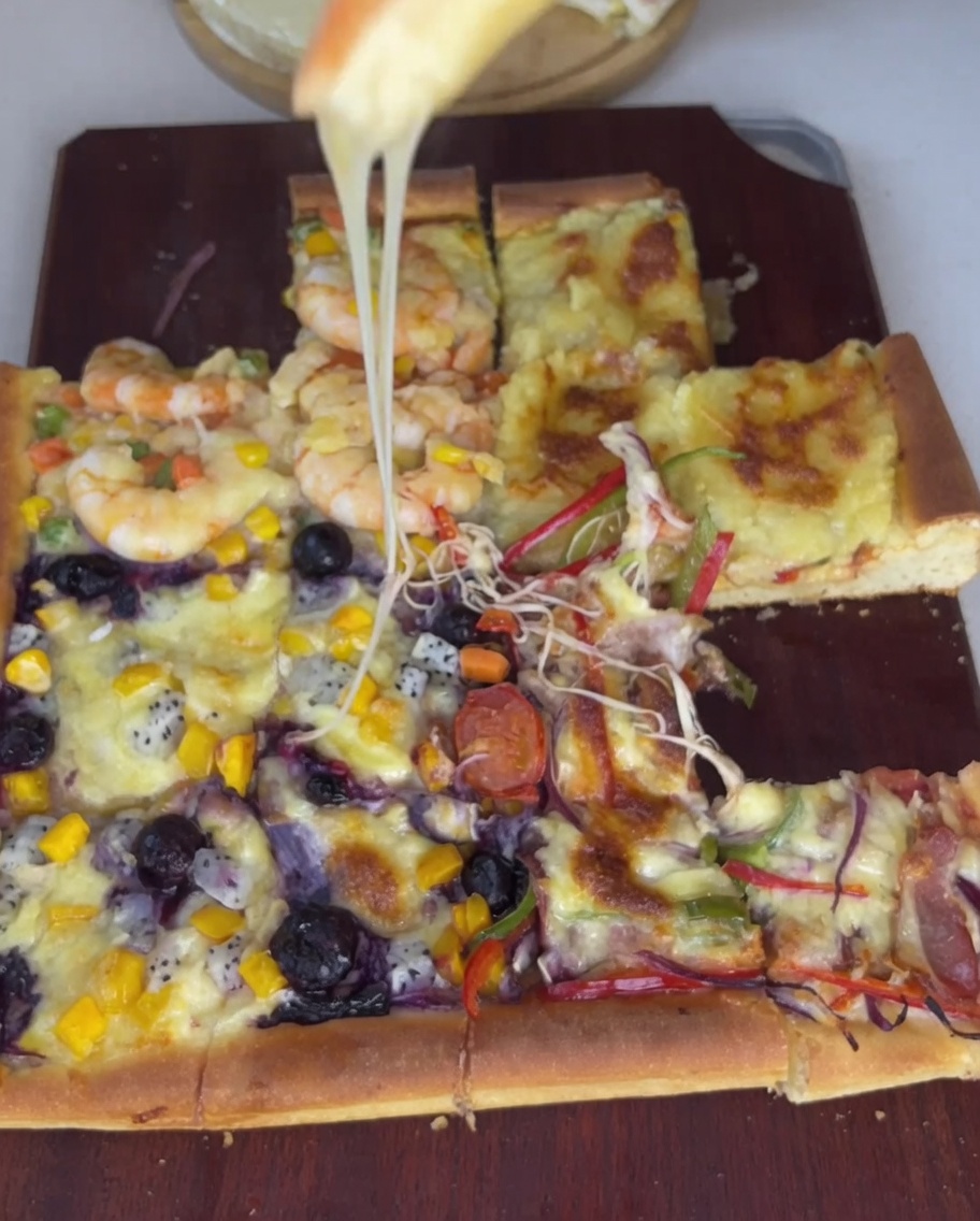 Close-up of bacon strips, red onions, and colorful bell peppers being carefully arranged on the pizza dough quadrant.