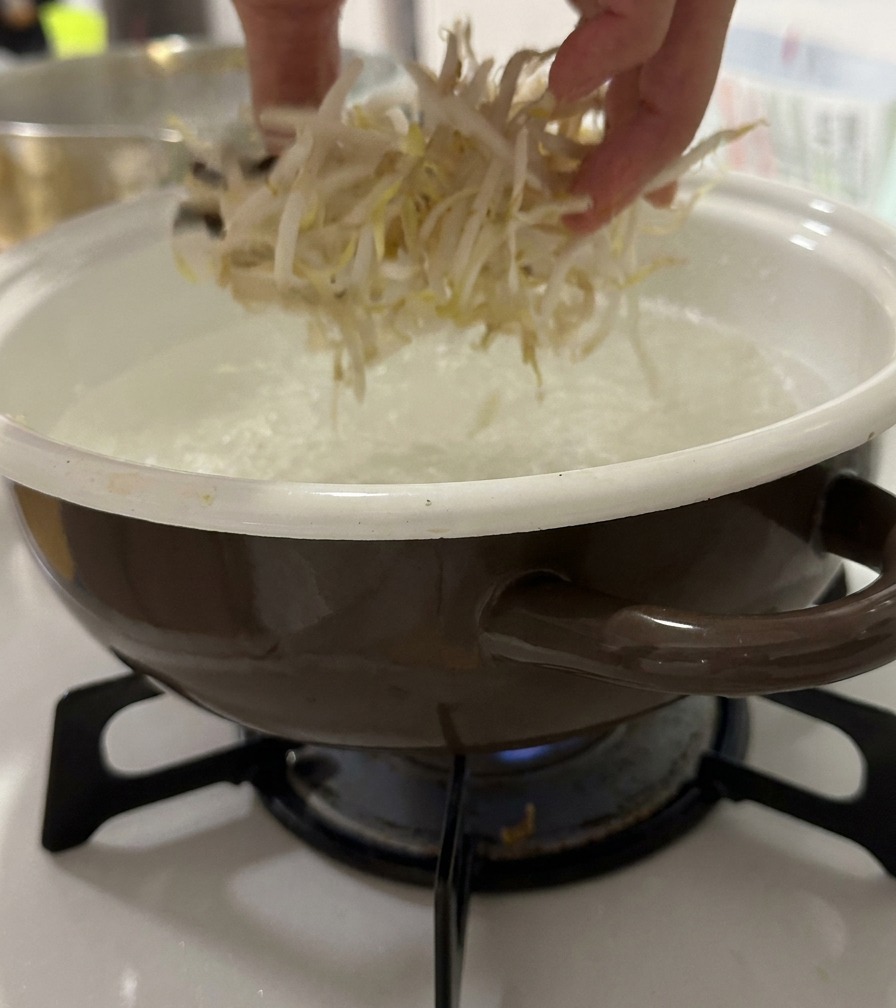 A hand dropping fresh bean sprouts into a pot of boiling water.