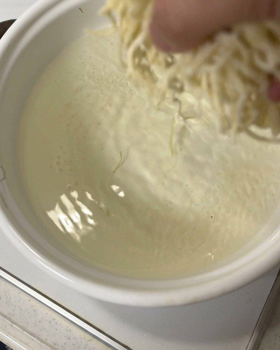A hand dropping a portion of fresh ramen noodles into a pot of rapidly boiling water.