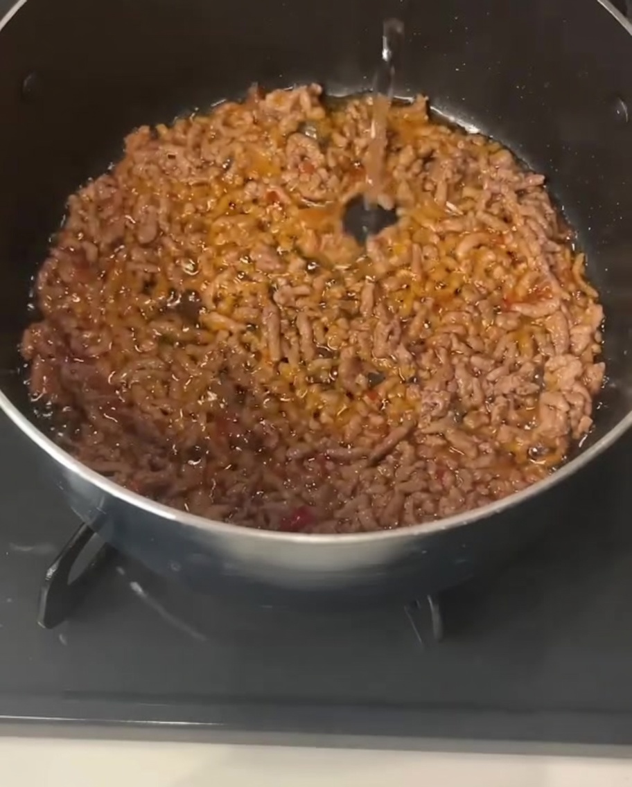 Clear liquid being poured into a pot containing cooked, seasoned ground pork.