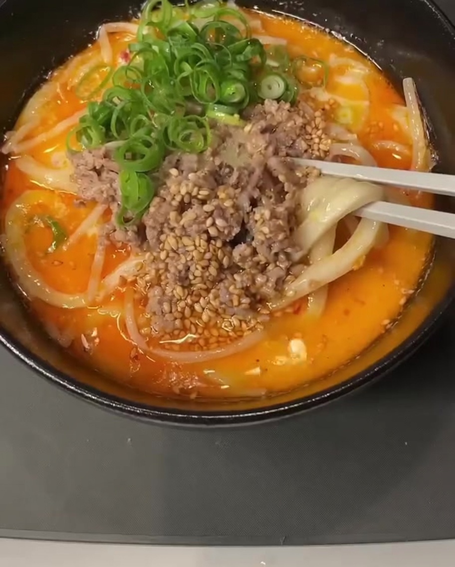 A close-up view of a pot containing a creamy liquid mixture with a spoonful of miso paste being stirred in.