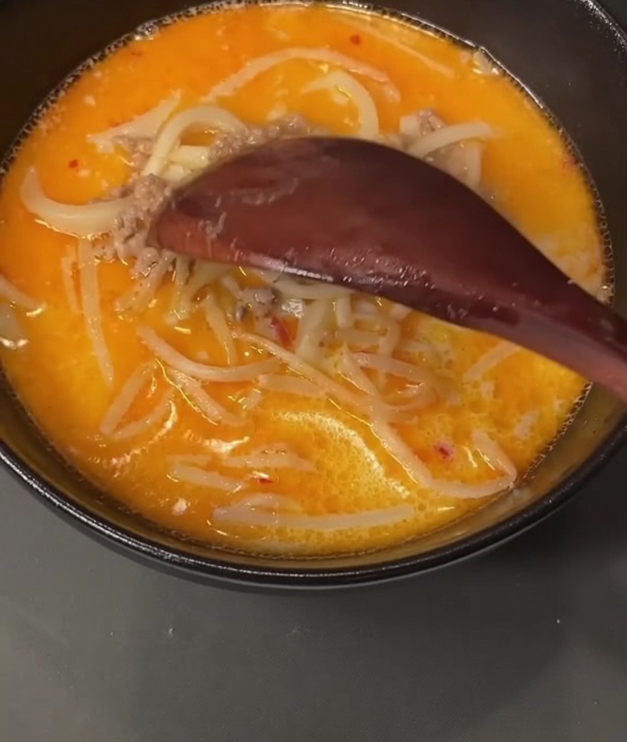A wooden spoon scooping cooked ground pork from a broth-filled pot.