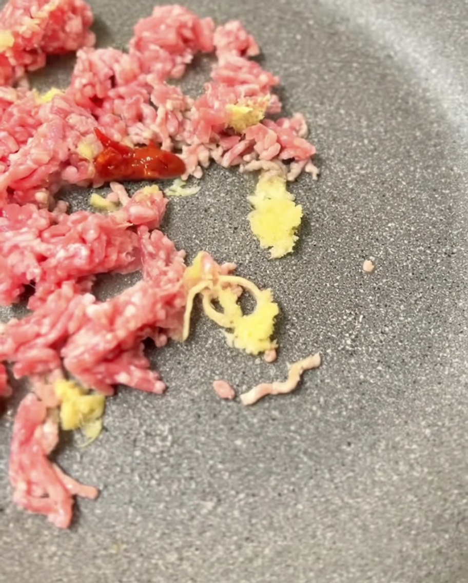 Miso bean paste being mixed into the browned pork in a frying pan.