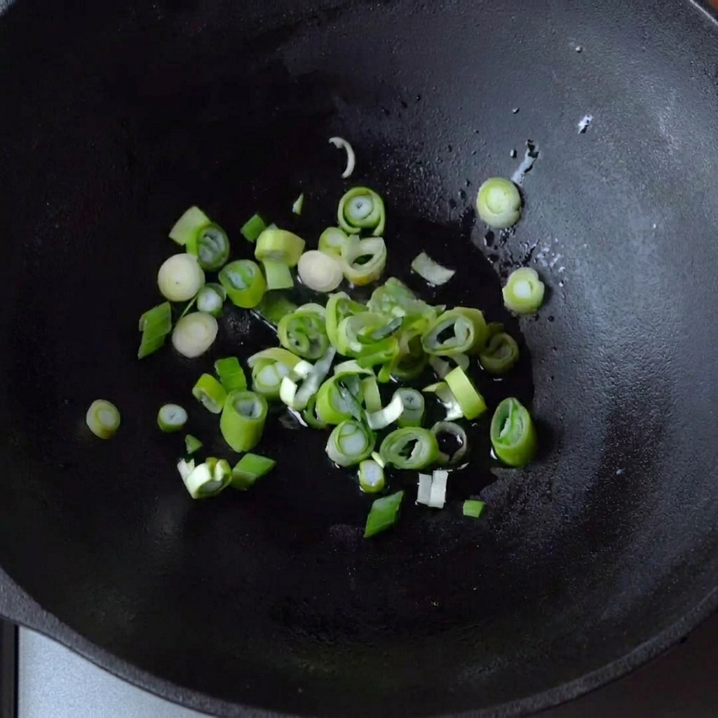 Green onions sizzling in a small amount of oil in a cast iron wok.