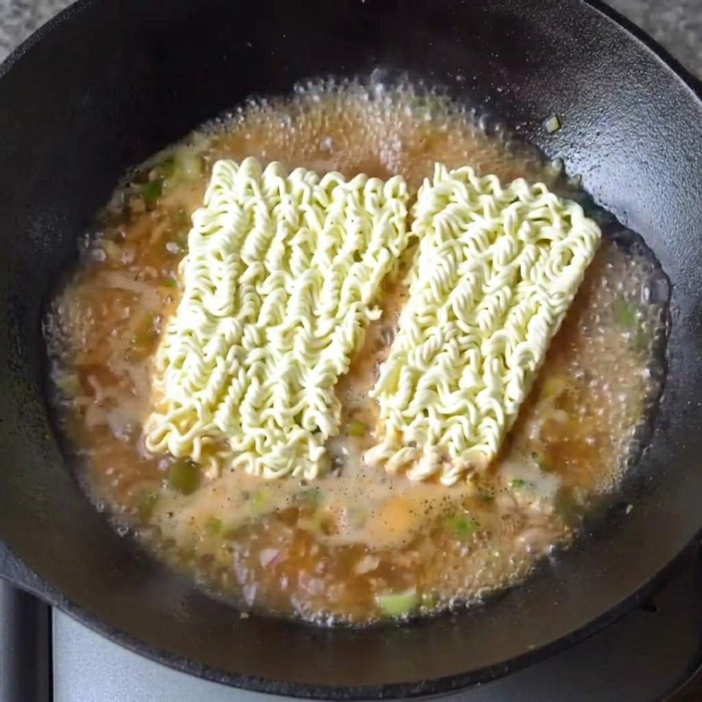 Two blocks of dried ramen noodles resting in the boiling, flavorful broth.