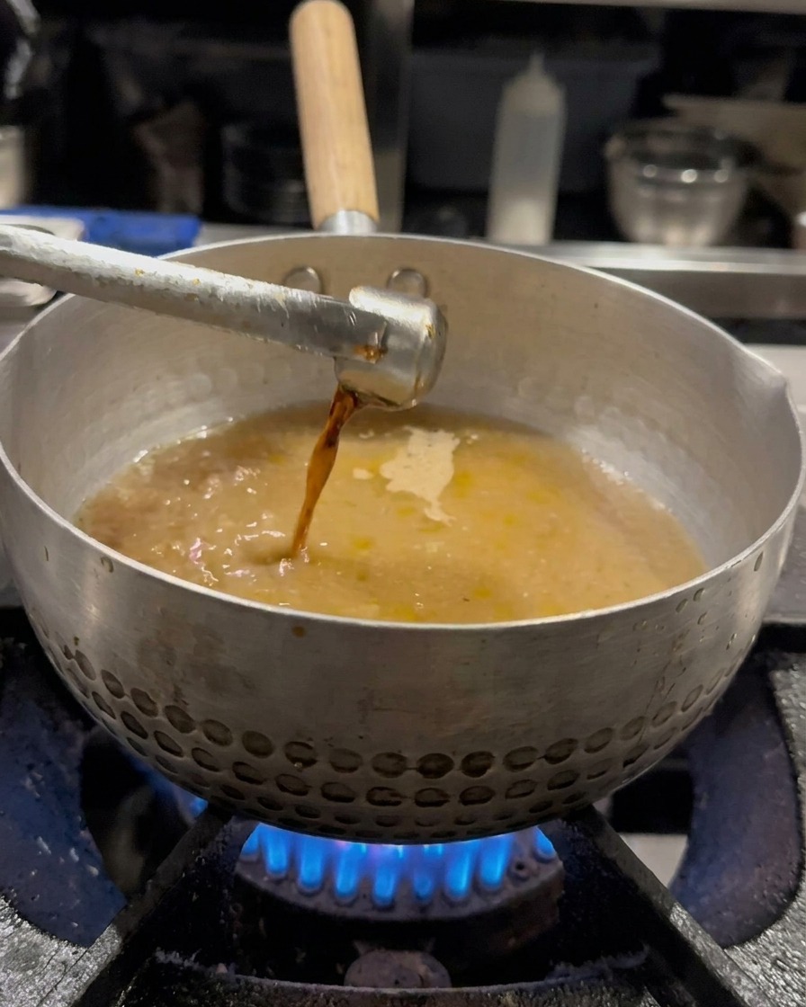 Soy sauce being drizzled into the broth-filled pot and mixed with a whisk.