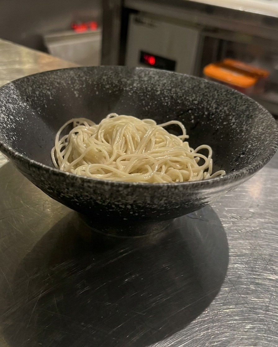 Cooked noodles in a black bowl being topped with rich, creamy hot broth.