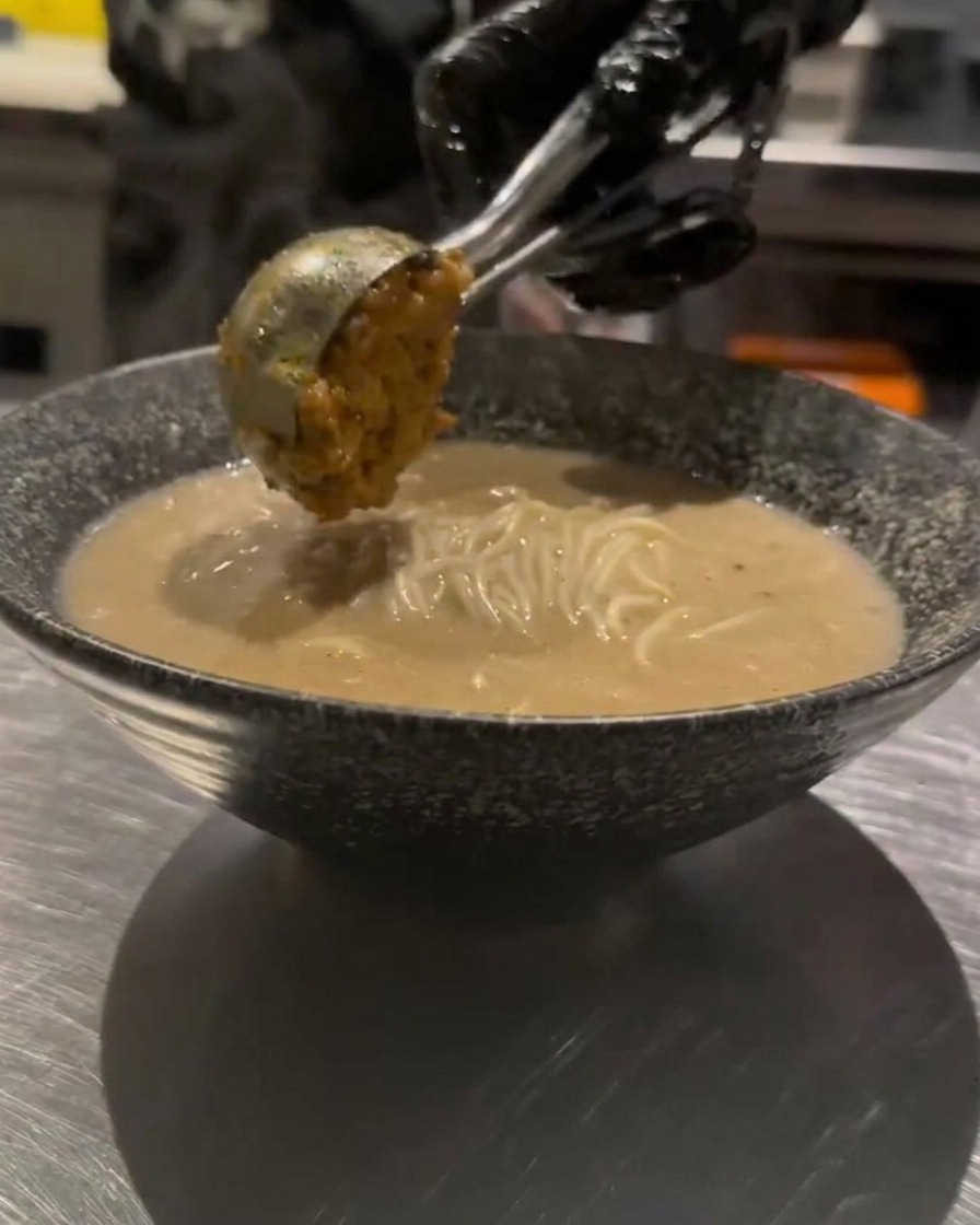 A spoonful of seasoned minced meat being carefully added on top of the ramen.