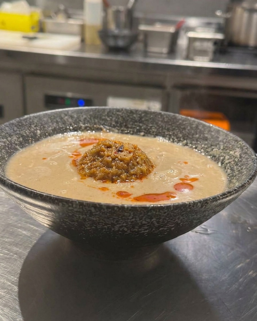 A bowl of Japanese-style Tan Tan Ramen with creamy broth, topped with a mound of minced meat and bright red chili oil drizzled on top.
