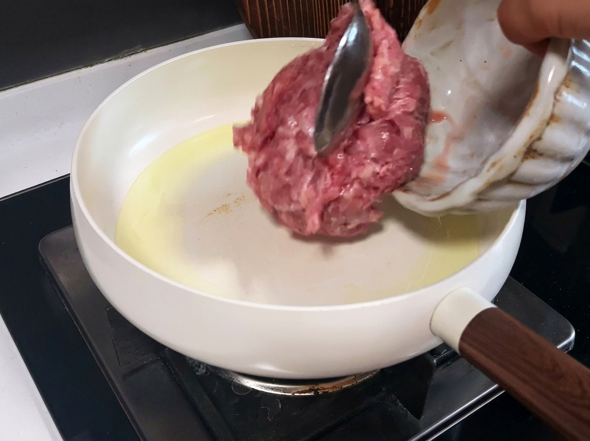 Ground pork cooking in a white pan, showing browned, cooked pieces.