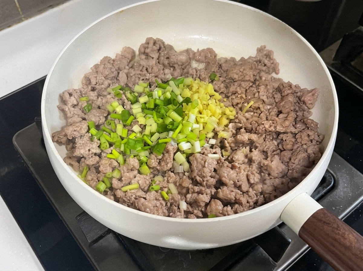 Ground pork in a pan being mixed with minced aromatics, bean paste, and soybean paste.