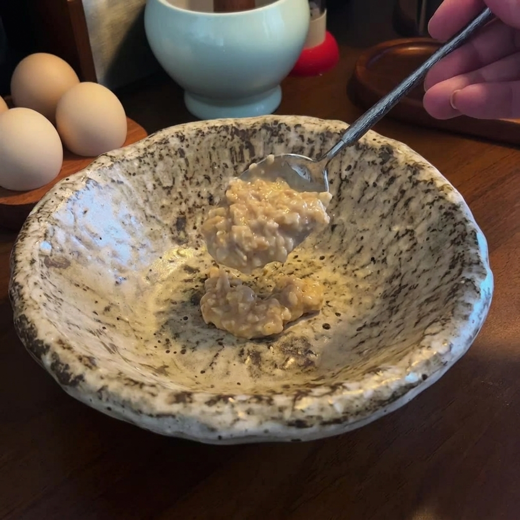 A spoonful of thick miso and sesame paste being added to an empty speckled ceramic serving bowl.