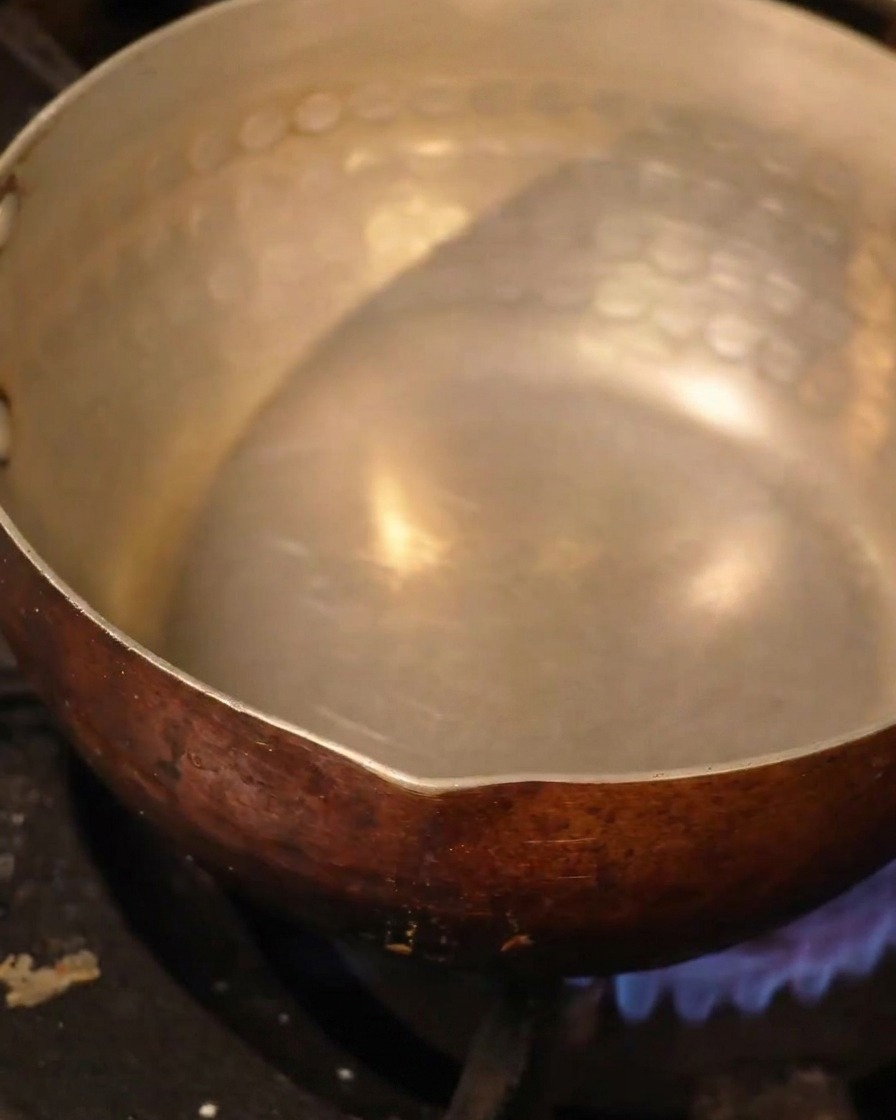 A hammered metal pot filled with liquid heating over a stove burner.