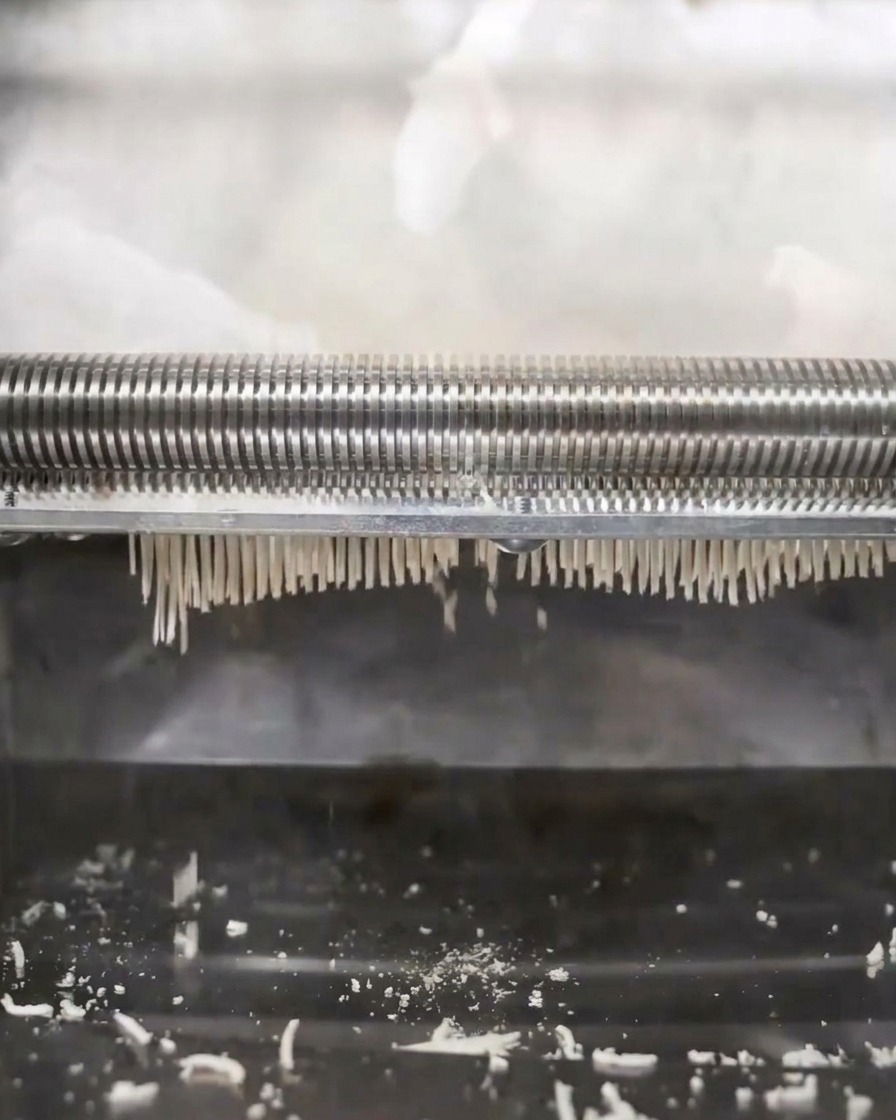 Noodle machine pressing and cutting dough into thin ramen strands.