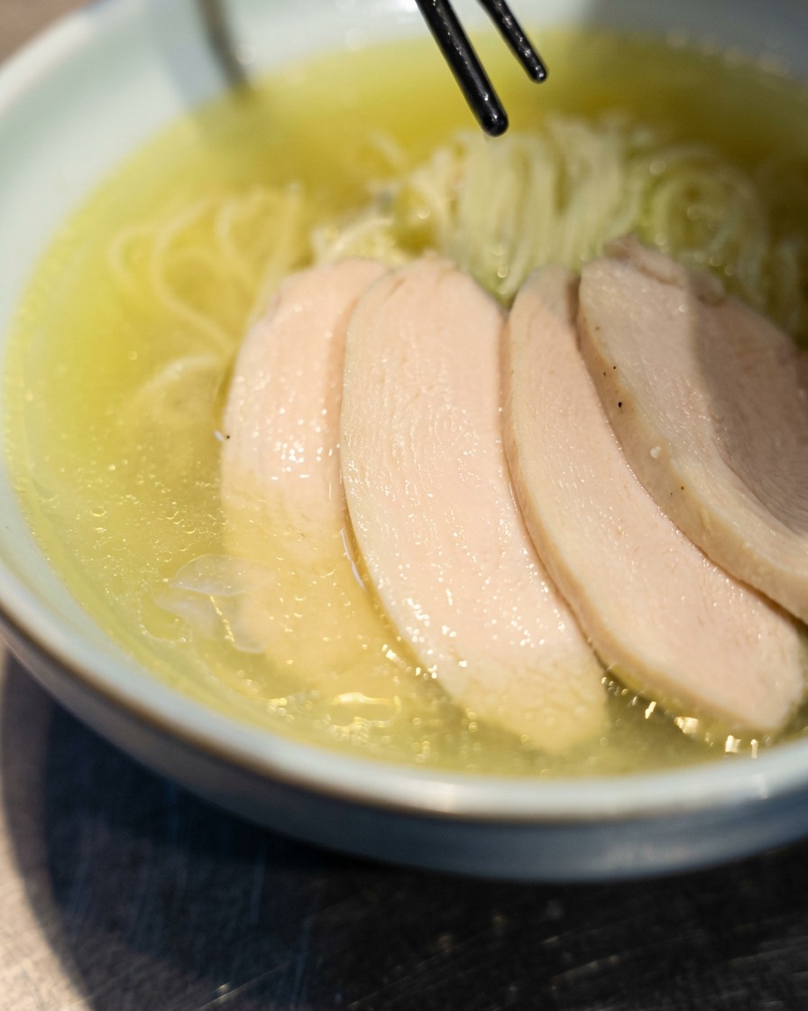Chopsticks placing slices of tender chicken chashu over freshly prepared ramen in a bowl.