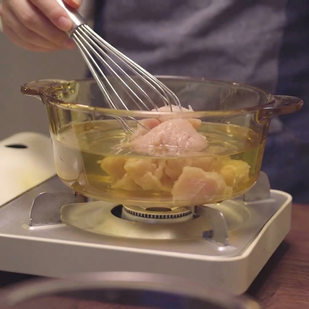 A whisk stirring minced chicken breast into the liquid within a glass pot.