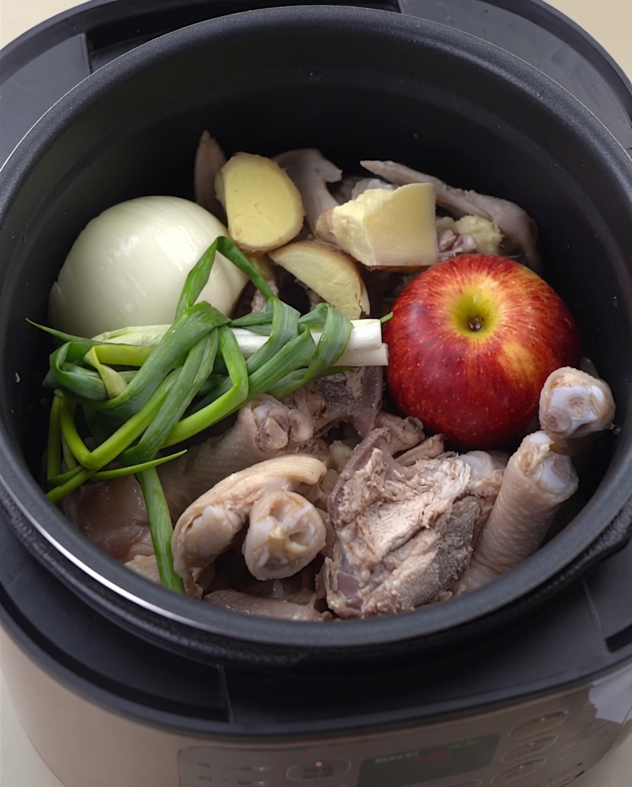 Water being poured into the pressure cooker over the chicken and aromatics.