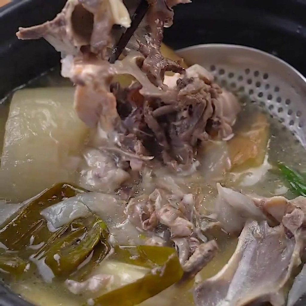 Tender chicken meat being pulled away from the cooked bones in the pressure cooker pot using black chopsticks.
