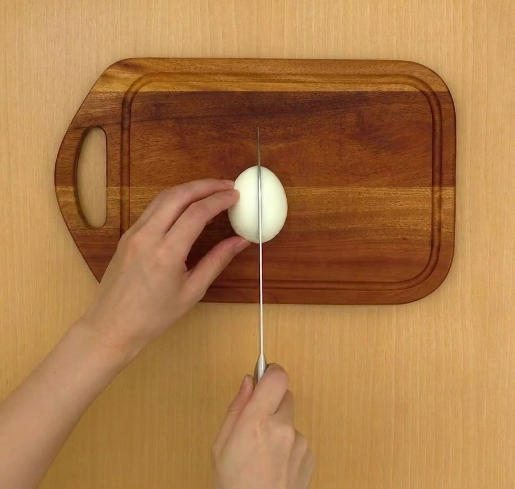 A soft-boiled egg being cut cleanly in half on a wooden cutting board.
