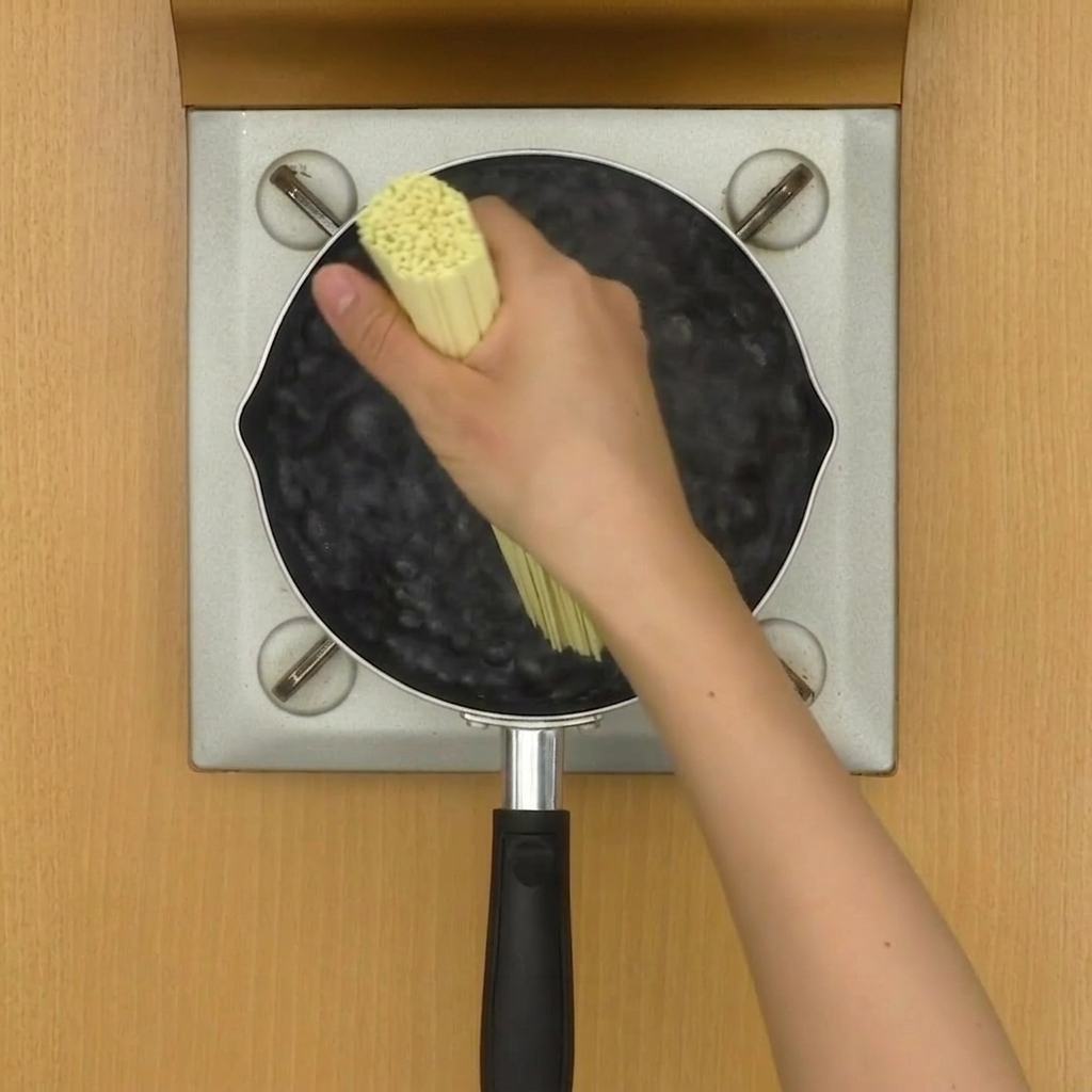 Ramen noodles boiling in a pot of water, being stirred by chopsticks.