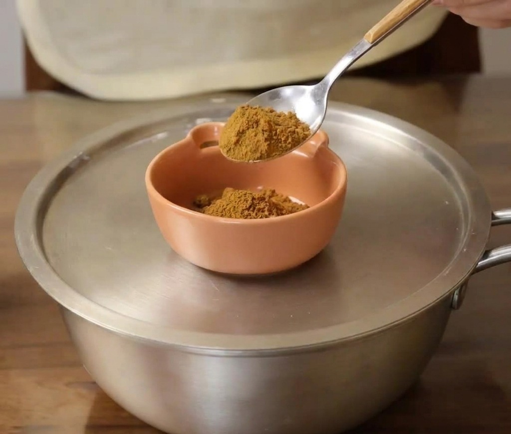 A spoonful of mustard powder being added to a small orange ceramic bowl.