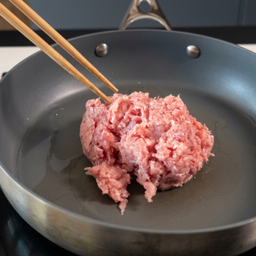 Minced pork being stirred in a non-stick pan with chopsticks.