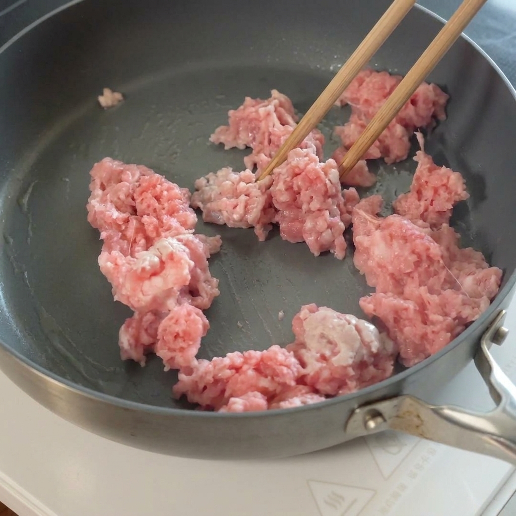 Sliced garlic being added to the cooked minced pork in the pan.
