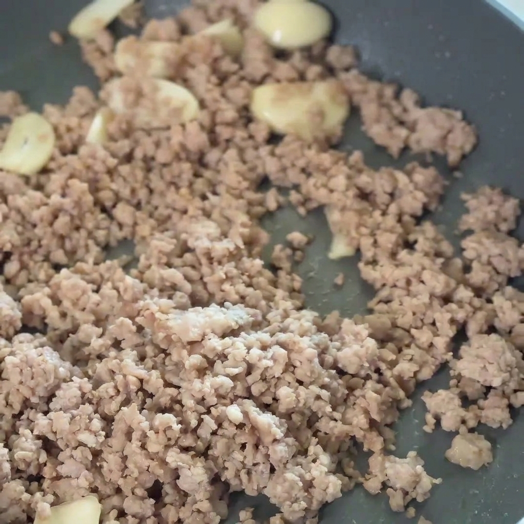 Red chili paste being stirred into the pork and garlic mixture.