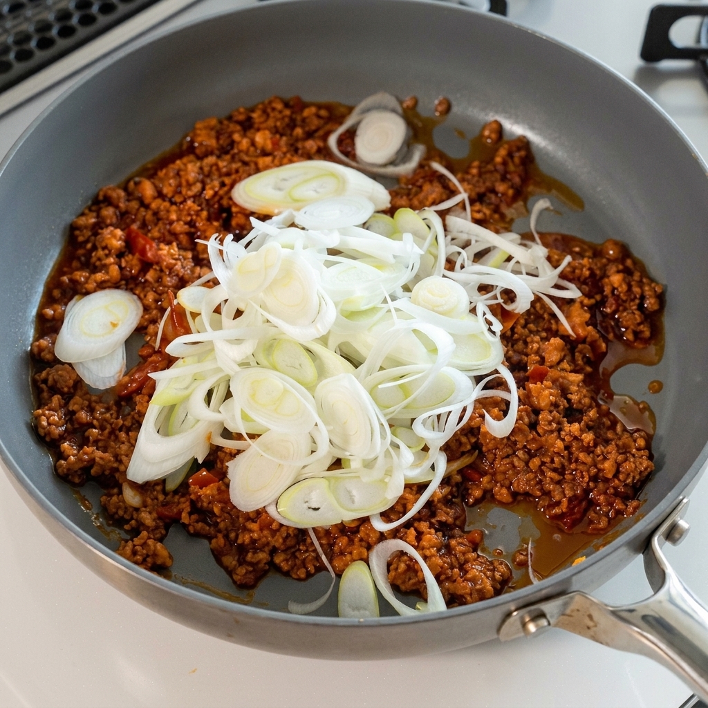 A large pile of sliced green onions being added to the meat sauce.