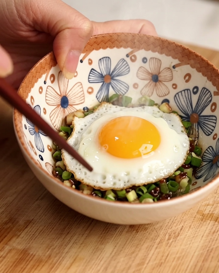 Ginger, scallions, and peppercorns being stirred in a bowl of water with chopsticks.