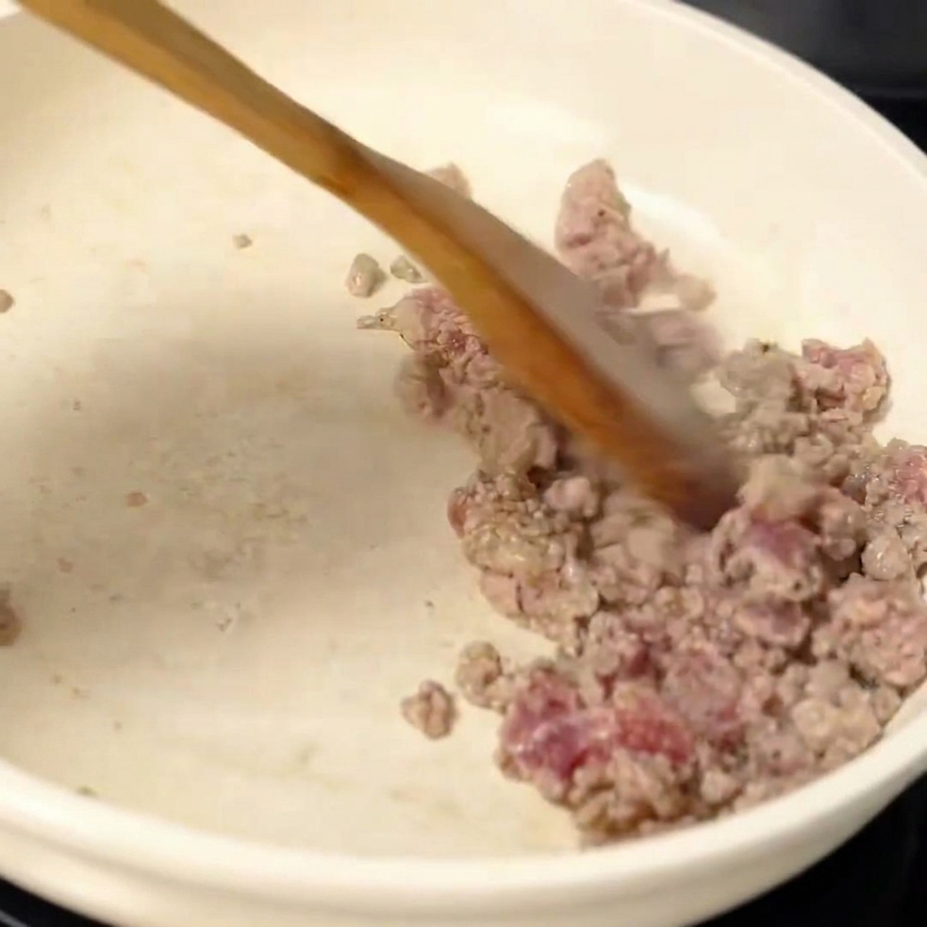 Browned minced pork being stirred in a pan as aromatics are incorporated.