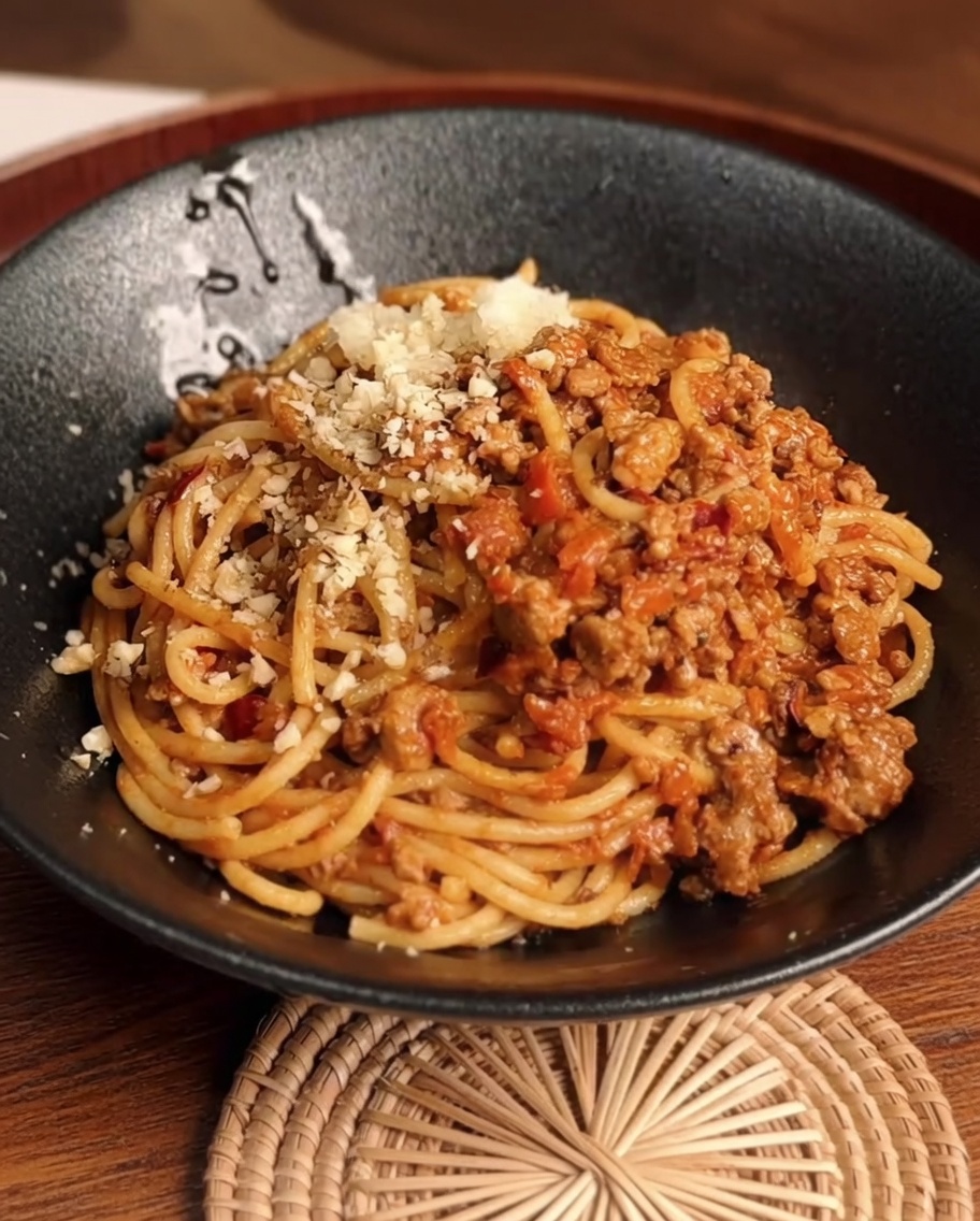 A mixture of ginger-scallion water and sesame paste being added to the cooked minced pork in a pan.