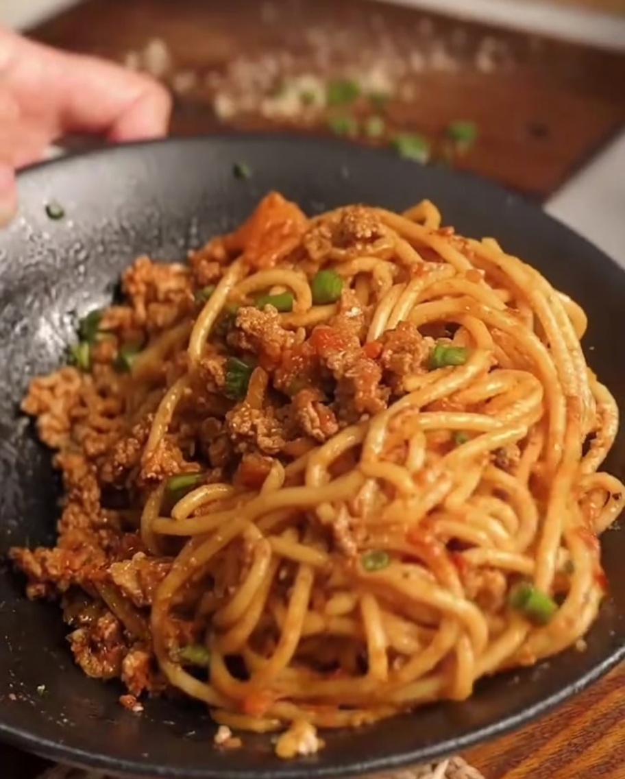 Freshly cooked spaghetti being placed into the pan containing the prepared meat and carrot sauce.