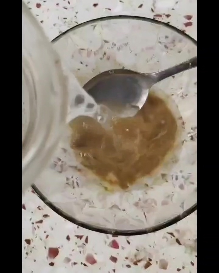 A small glass bowl containing a thick brown sauce being stirred with a metal spoon.