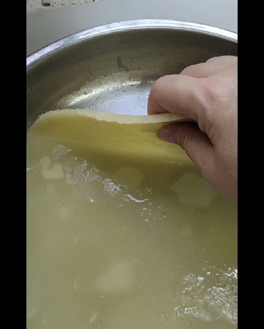 A hand placing a sheet of rolled dough onto a shiny metal tray.