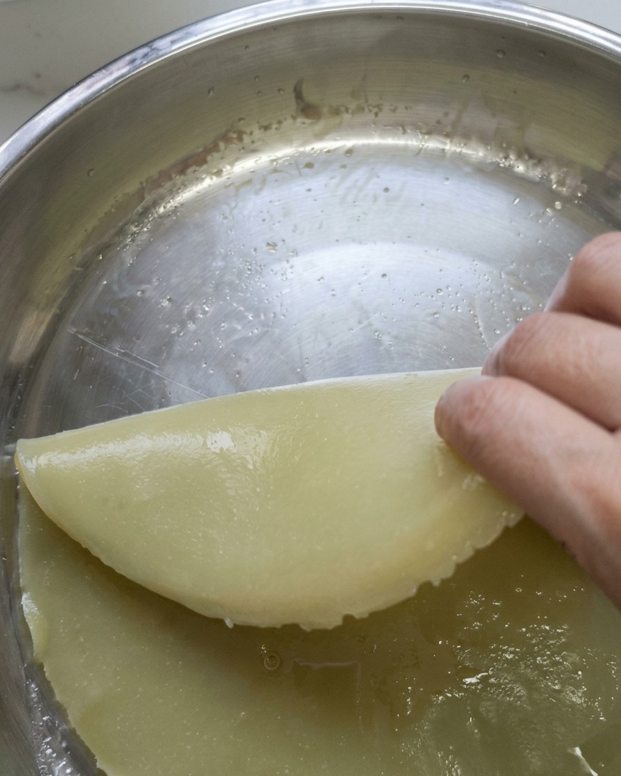 A steamed piece of dough being sliced into long, even strips on a board.