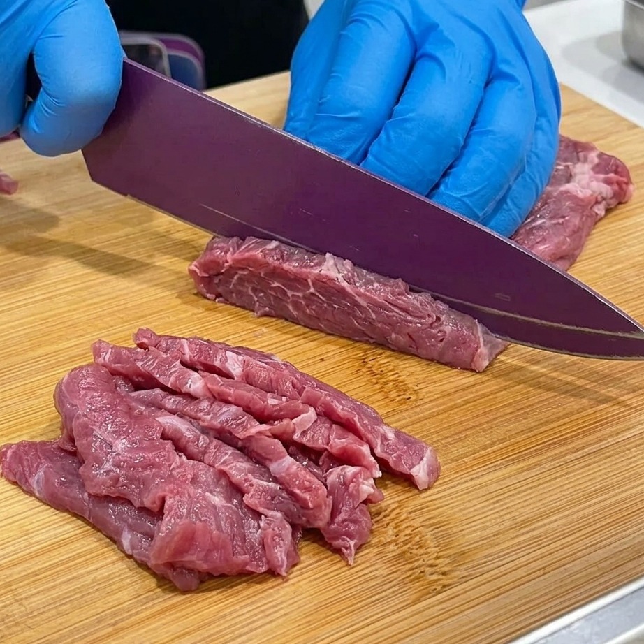 Close-up of beef chuck being sliced thinly on a wooden cutting board.