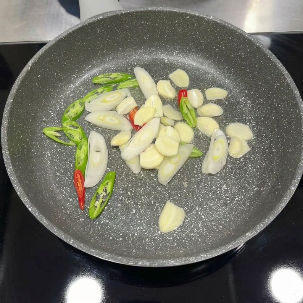 Sliced garlic, chili, and green onions cooking in a pan until aromatic.